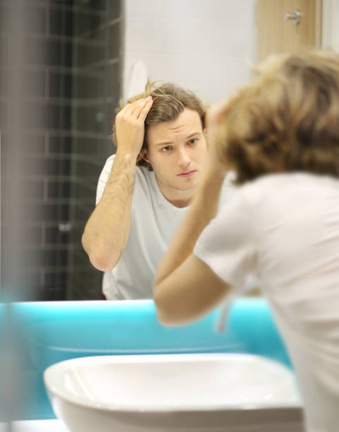 istock young man looking in the mirror,combing his hair,looking at problems on face 1204696428