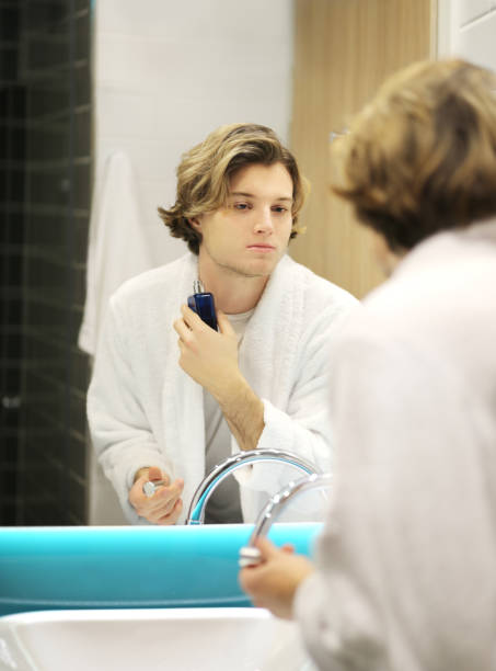 istock young man looking in the mirror,combing his hair,looking at problems on face 1204696433