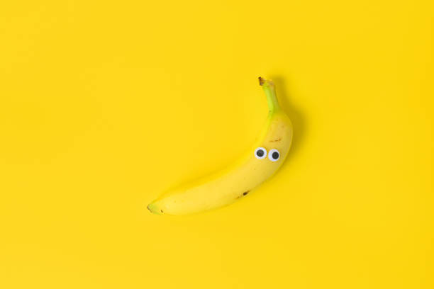 This is a color photograph of a banana with googly eyes on a bright colored background.