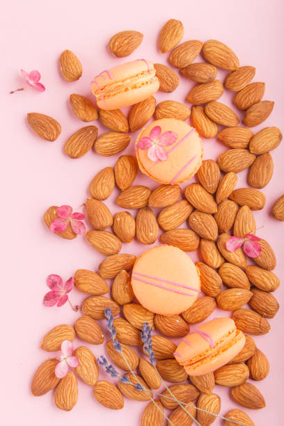 Orange macarons or macaroons cakes with almond nuts on pastel pink background. top view, flat lay, close up.