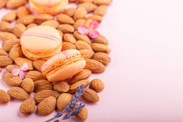 Orange macarons or macaroons cakes with almond nuts on pastel pink background. side view, close up, selective focus, copy space.