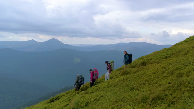 The four active people with backpacks walking down on the mountain