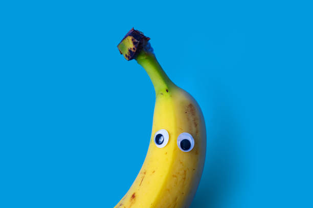 This is a color photograph of a banana with googly eyes on a bright colored background.