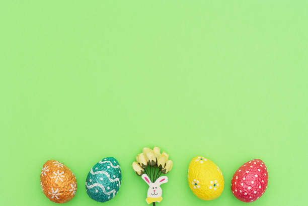 istock Colorful painted orange, blue, red and yellow Easter eggs with Easter rabbit and yellow spring flowers on green background. Happy Easter holiday concept. Flat lay style with copy space. 1204713247