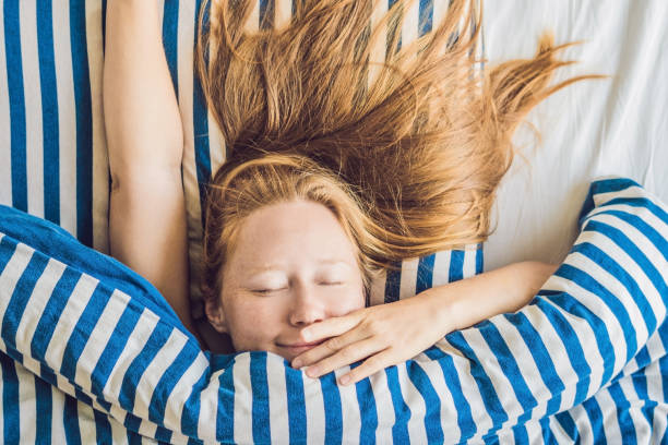 belle jeune femme se couchant dans le lit et dormant. ne pas obtenir assez concept de sommeil - beauty beautiful tired blond hair photos et images de collection