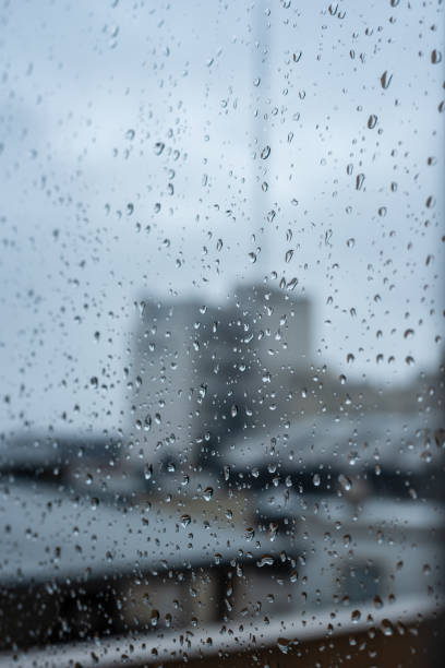 istock Window on a rainy day with small drops in it. Focus on the small drops with shallow depth of field and a visual of city buildings. 1204718812