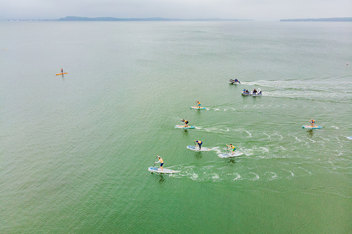 Strong men floating on a SUP boards in a beautiful bay on a sunny day. Aerial view of the men crosses the bay using the paddleboard. Water sports, competitions.