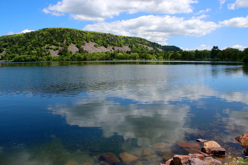 Devil's Lake State Park landscape with view on the East Bluff hiking trail hill behind a lake water with cloudy blue sky reflection. Baraboo area, Wisconsin, Midwest USA.