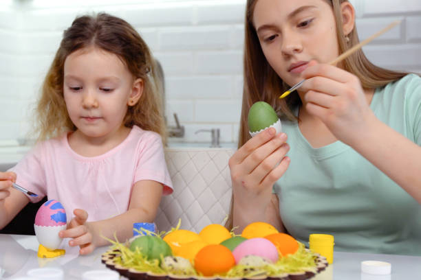 istock Happy easter. Two sisters painting Easter eggs. Happy family children preparing for Easter. Cute little child girl wearing bunny ears on Easter day 1204736453