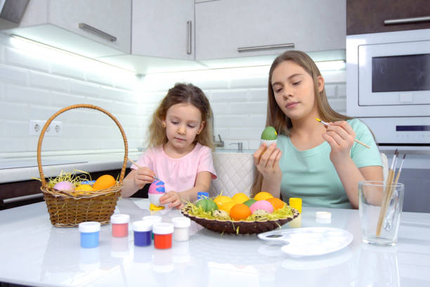 istock Happy easter. Two sisters painting Easter eggs. Happy family children preparing for Easter. Cute little child girl wearing bunny ears on Easter day 1204736958