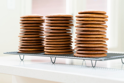 Three freshly baked stacks of gingernut cookies on domestic kitchen bench