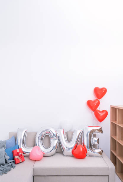 foil love balloons and gifts on a sofa with white wall in background for valentine's day, mother's day surprise. - cushion pillow heart shape multi colored imagens e fotografias de stock