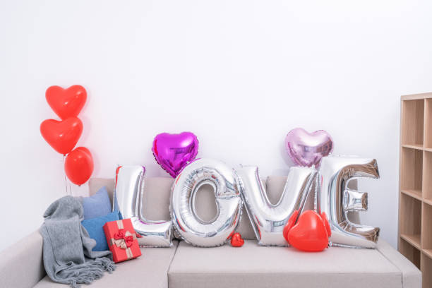 foil palloncini d'amore e regali su un divano con parete bianca sullo sfondo per san valentino, sorpresa festa della mamma. - cushion pillow heart shape multi colored foto e immagini stock