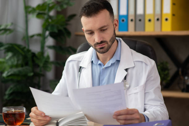 istock Dark-haired bearded doctor in a white robe working with reports 1204763084
