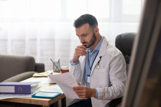 istock Dark-haired bearded doctor in a white robe looking concentrated 1204763098