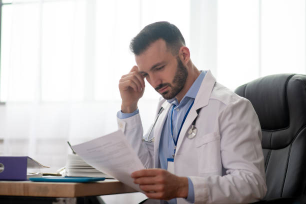 istock Young bearded doctor in a white robe reading 1204763102