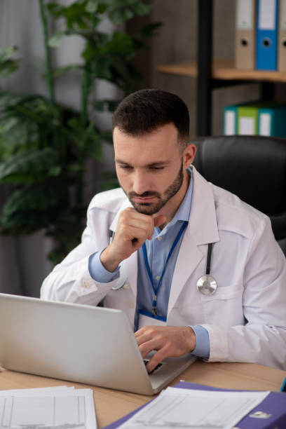 istock Young bearded doctor looking serious working on laptop 1204763148