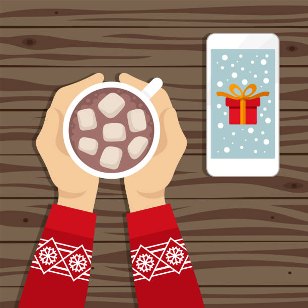 stockillustraties, clipart, cartoons en iconen met handen met cacaodrank en telefoon met gift op het scherm dat op houten lijst legt - cafe snow