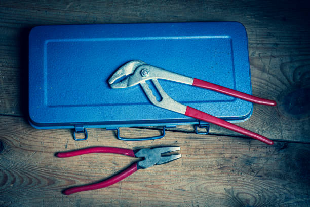 Pliers and a metallic tool box on a wooden box in front of a dark background