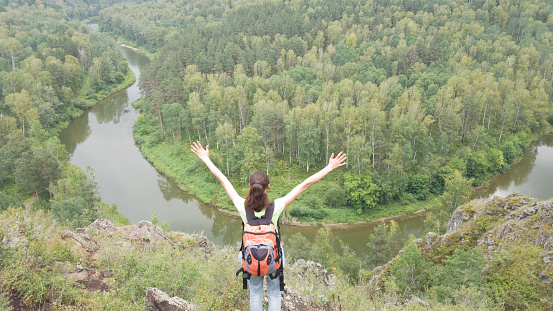 A female traveler stands with a backpack hands up. Success, luck, achievement. Travel to the Berd rocks in Russia. Novosibirsk region, summer.