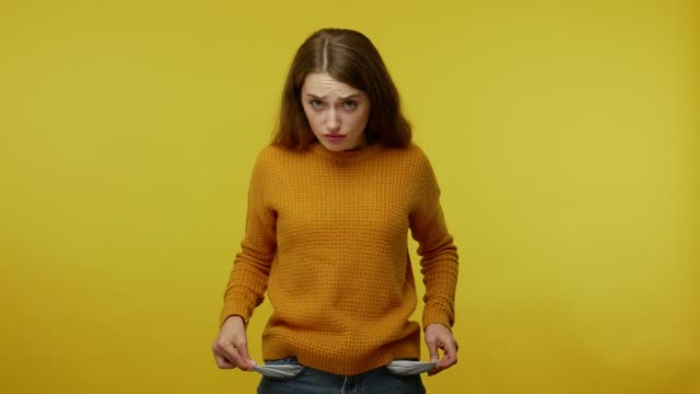 Frustrated upset poor girl with brown hair in pullover turning out pockets gesturing no money