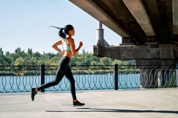 istock Sporty woman running outdoors by river 1204779410