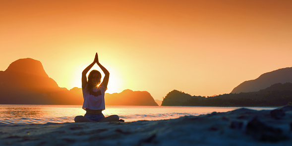 Silhouette young woman practicing yoga on the beach at sunset. Health and meditation concept