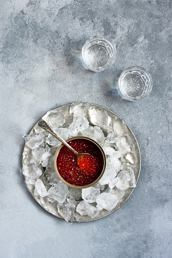 Red caviar in  can on ice and  vodka in shot glass  on concrete background. Top view with copy space