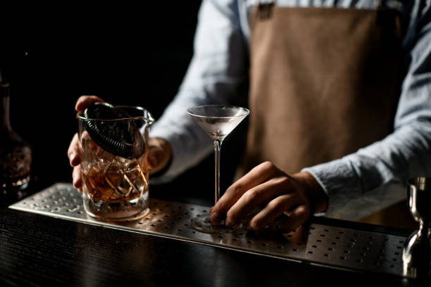 istock Professional bartender holding a little martini glass and measuring cup with a cocktail 1204783343
