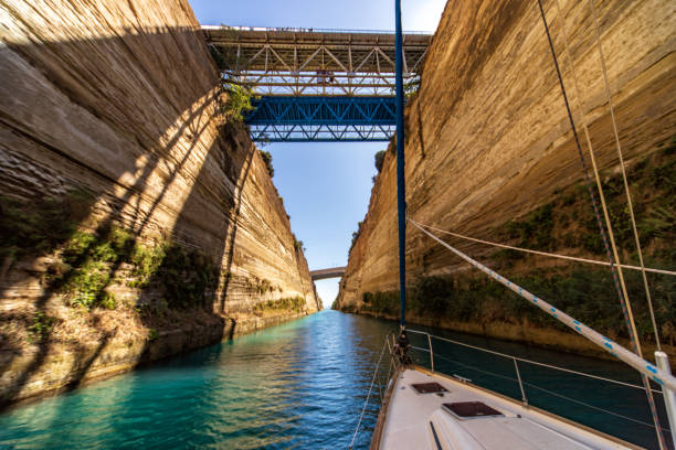 Sailboat sailing through Corinth canal. This amazing landmark connecting Ionian sea with Aegean sea and separate Peloponnese from Greece mainland. Photo taken from the deck, from the boat perspective.