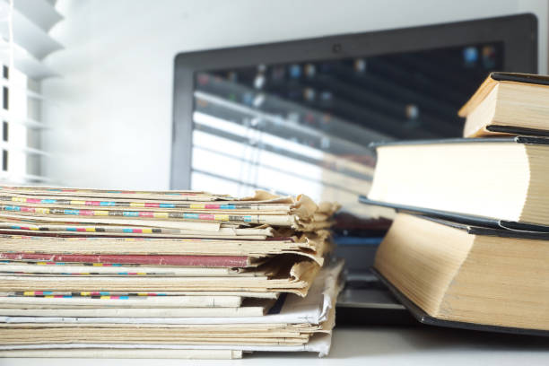 istock Open Laptop with Books and Newspapers Stacked on its Keyboard 1204790489
