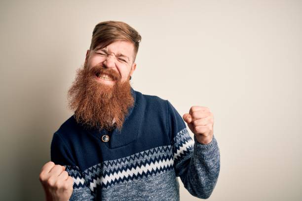 homme rouge irlandais bel avec la barbe utilisant le chandail d’hiver au-dessus du fond isolé très heureux et excité faisant le geste gagnant avec des bras levés, souriant et criant pour le succès. concept de célébration. - men sweater excitement satisfaction photos et images de collection