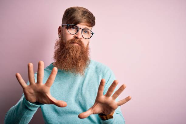 istock Handsome Irish redhead man with beard wearing glasses over pink isolated background Moving away hands palms showing refusal and denial with afraid and disgusting expression. Stop and forbidden. 1204794749