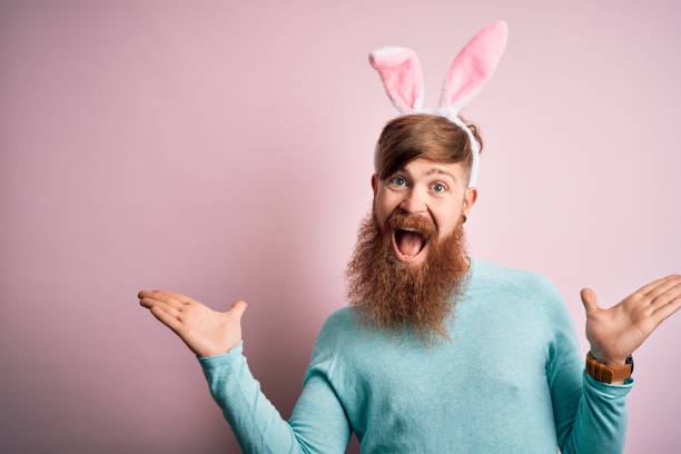 Hipster Irish man with beard wearing easter rabbit ears over isolated pink background celebrating crazy and amazed for success with arms raised and open eyes screaming excited. Winner concept