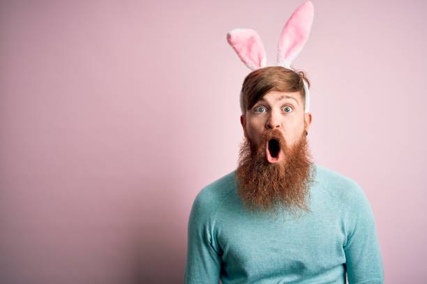 istock Hipster Irish man with beard wearing easter rabbit ears over isolated pink background afraid and shocked with surprise expression, fear and excited face. 1204794763