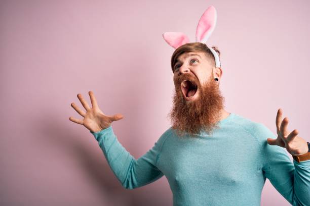 istock Hipster Irish man with beard wearing easter rabbit ears over isolated pink background crazy and mad shouting and yelling with aggressive expression and arms raised. Frustration concept. 1204794772