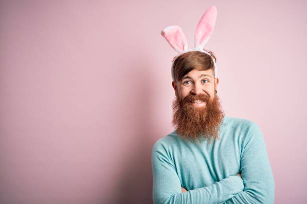 istock Hipster Irish man with beard wearing easter rabbit ears over isolated pink background happy face smiling with crossed arms looking at the camera. Positive person. 1204794779