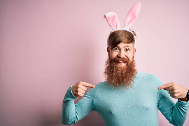 istock Hipster Irish man with beard wearing easter rabbit ears over isolated pink background looking confident with smile on face, pointing oneself with fingers proud and happy. 1204794797