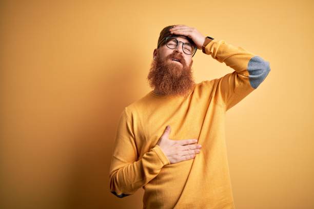 istock Handsome Irish redhead man with beard wearing glasses over yellow isolated background Touching forehead for illness and fever, flu and cold, virus sick 1204794877