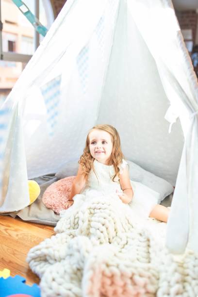 istock Adorable blonde toddler playing sitting on blanket inside tipi at kindergarten 1204796336