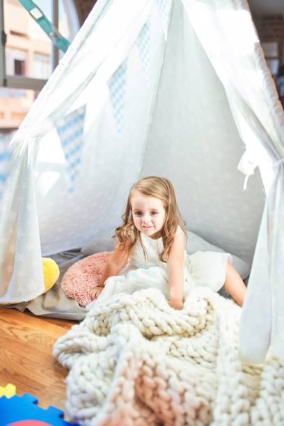 istock Adorable blonde toddler playing sitting on blanket inside tipi at kindergarten 1204796347