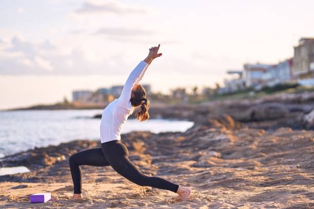 istock Young beautiful sportwoman practicing yoga. Coach teaching warrior pose at the beach 1204796603