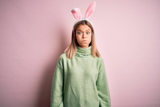 istock Young beautiful woman wearing easter rabbit ears standing over isolated pink background puffing cheeks with funny face. Mouth inflated with air, crazy expression. 1204797690