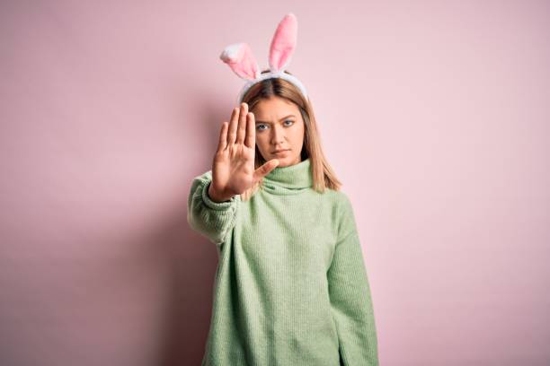 istock Young beautiful woman wearing easter rabbit ears standing over isolated pink background doing stop sing with palm of the hand. Warning expression with negative and serious gesture on the face. 1204797696
