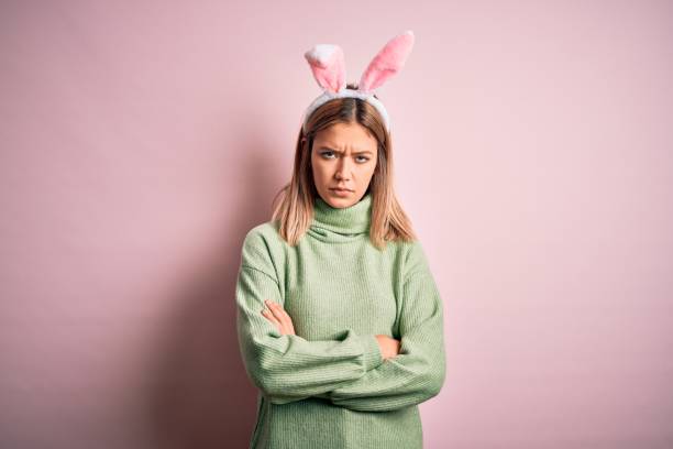 istock Young beautiful woman wearing easter rabbit ears standing over isolated pink background skeptic and nervous, disapproving expression on face with crossed arms. Negative person. 1204797697