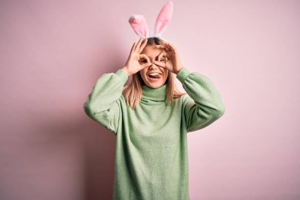 istock Young beautiful woman wearing easter rabbit ears standing over isolated pink background doing ok gesture like binoculars sticking tongue out, eyes looking through fingers. Crazy expression. 1204797699