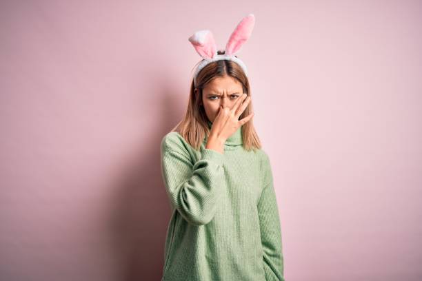 istock Young beautiful woman wearing easter rabbit ears standing over isolated pink background smelling something stinky and disgusting, intolerable smell, holding breath with fingers on nose. Bad smell 1204797722