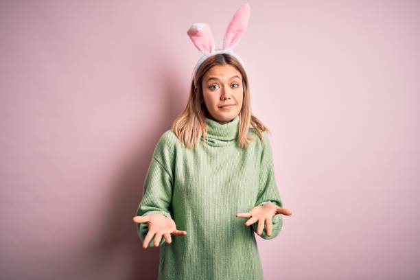 istock Young beautiful woman wearing easter rabbit ears standing over isolated pink background clueless and confused expression with arms and hands raised. Doubt concept. 1204797735