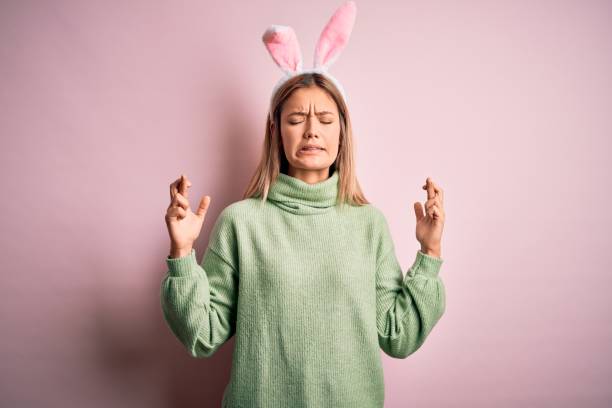 istock Young beautiful woman wearing easter rabbit ears standing over isolated pink background gesturing finger crossed smiling with hope and eyes closed. Luck and superstitious concept. 1204798255