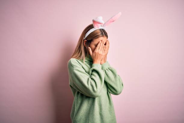 istock Young beautiful woman wearing easter rabbit ears standing over isolated pink background with sad expression covering face with hands while crying. Depression concept. 1204798270